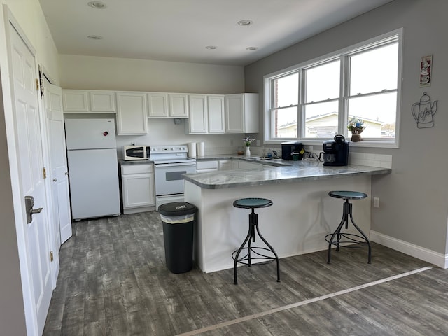 kitchen with white appliances, a peninsula, dark wood finished floors, and white cabinetry