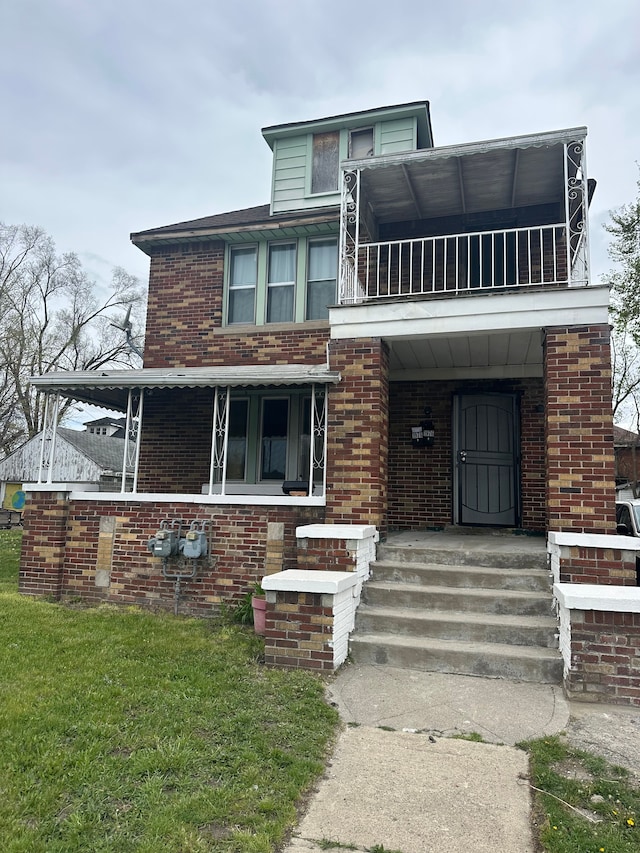 view of front facade featuring brick siding, a balcony, a front yard, and covered porch