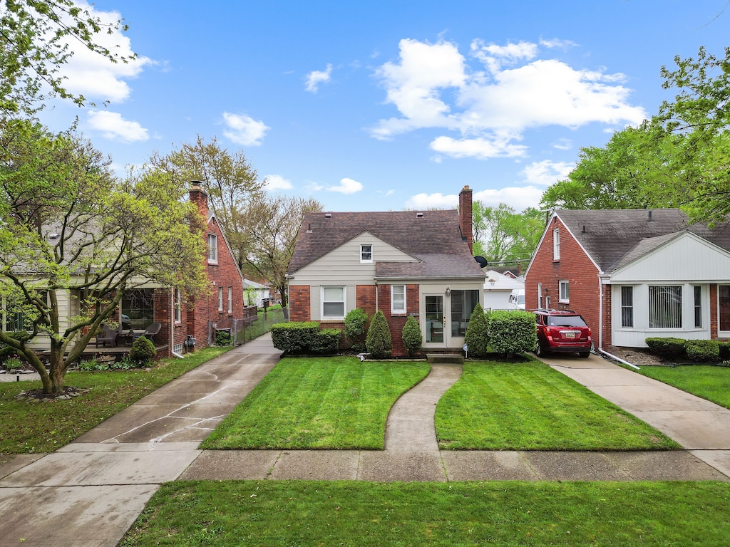 bungalow-style home featuring brick siding, concrete driveway, a front yard, and a chimney