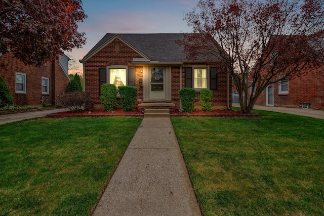 view of front of house with a lawn, roof with shingles, and brick siding