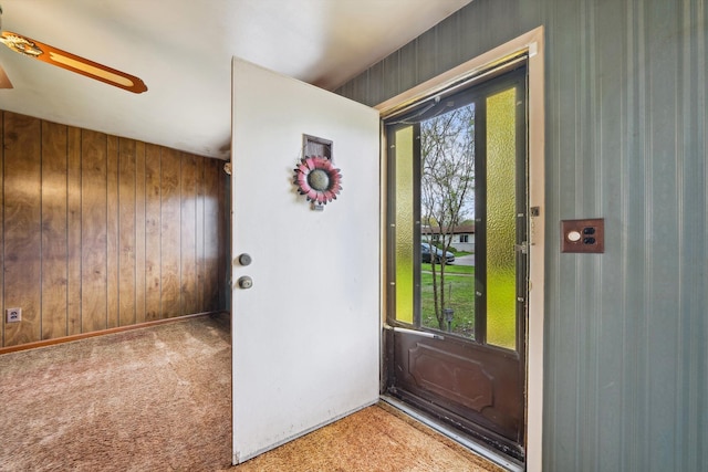 doorway to outside featuring ceiling fan, carpet, and wood walls