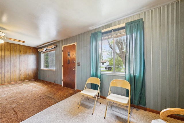 living area featuring carpet flooring, a ceiling fan, baseboards, and wood walls