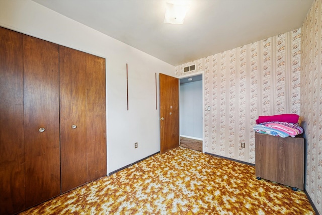 unfurnished bedroom with carpet, wallpapered walls, baseboards, visible vents, and a closet