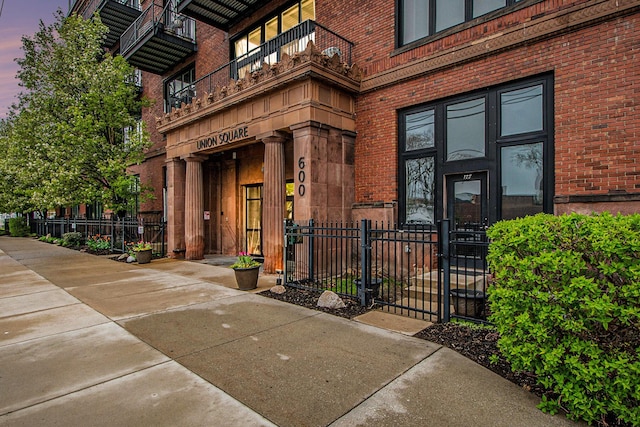 entrance to property featuring brick siding, a gate, fence, and a balcony