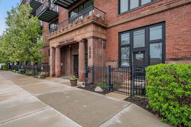 doorway to property with brick siding, fence, a gate, and a balcony