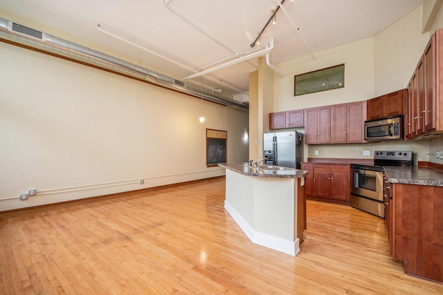 kitchen featuring track lighting, visible vents, a towering ceiling, dark countertops, and stainless steel appliances