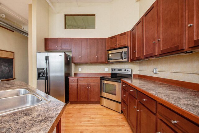 kitchen with a towering ceiling, dark countertops, a sink, light wood finished floors, and stainless steel appliances