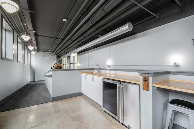 kitchen with a sink, finished concrete flooring, wine cooler, and white cabinetry