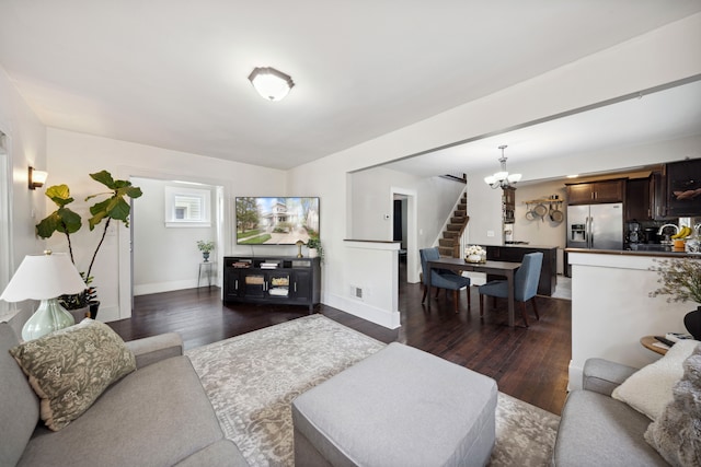 living area featuring an inviting chandelier, baseboards, visible vents, dark wood-style floors, and stairway