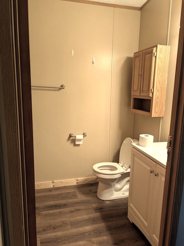 half bathroom featuring vanity, baseboards, toilet, and wood finished floors