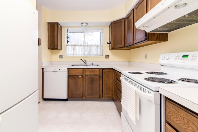 kitchen with a sink, light countertops, under cabinet range hood, and white appliances