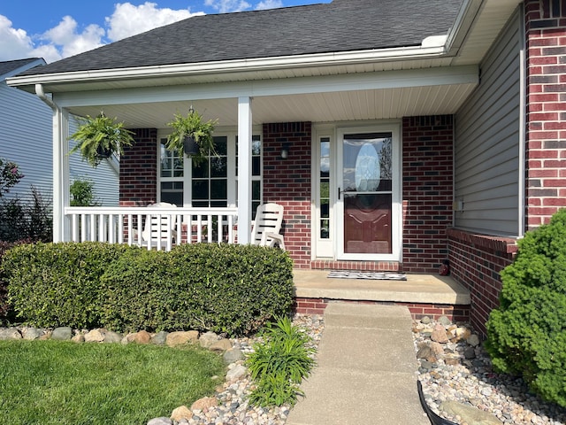doorway to property with brick siding, covered porch, and roof with shingles
