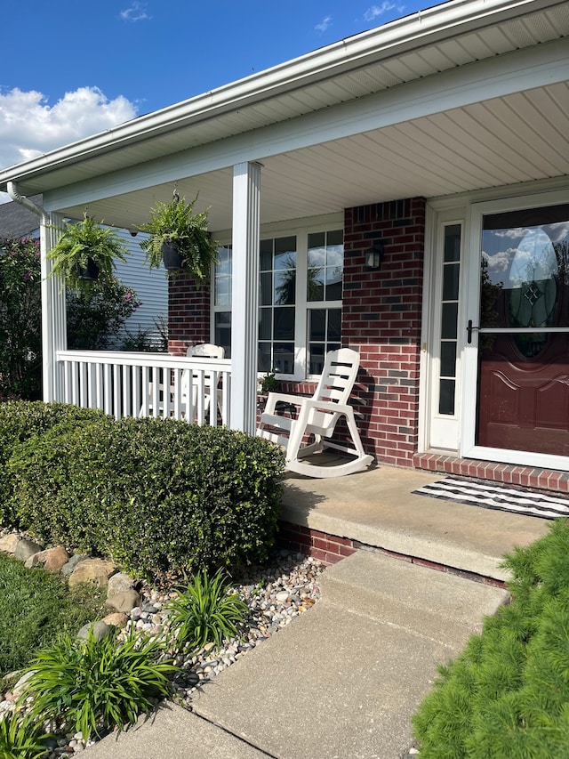 view of exterior entry with brick siding and covered porch