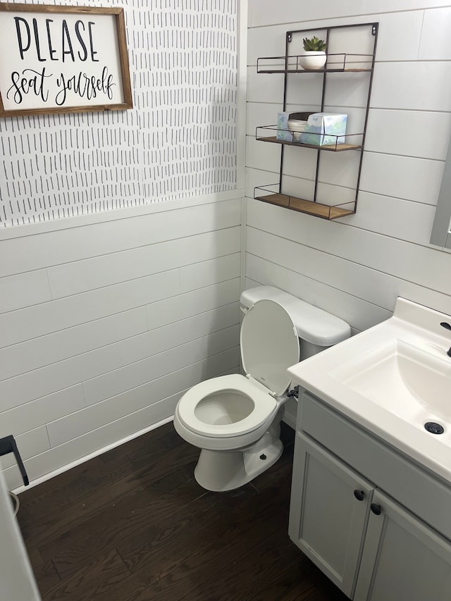 half bath with wood finished floors, toilet, vanity, and wooden walls