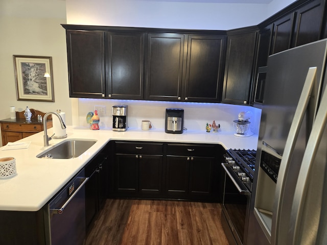 kitchen with a peninsula, light countertops, a sink, dark wood finished floors, and appliances with stainless steel finishes