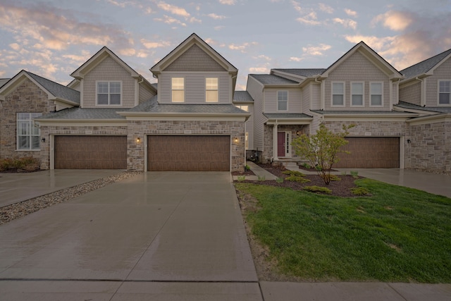 multi unit property with concrete driveway, a yard, a garage, and stone siding