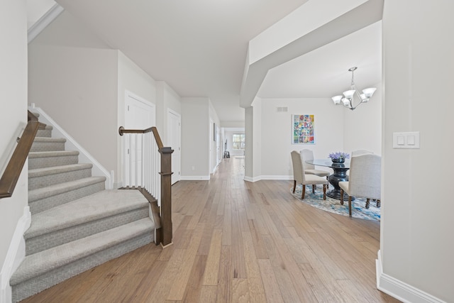 entryway featuring a notable chandelier, light wood-style flooring, baseboards, visible vents, and stairs