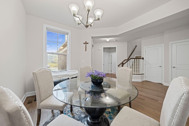dining area featuring an inviting chandelier, wood finished floors, baseboards, and stairs