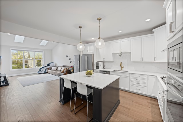 kitchen with a sink, a breakfast bar area, white cabinetry, open floor plan, and appliances with stainless steel finishes