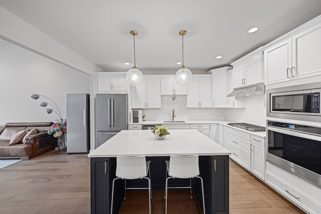 kitchen featuring a kitchen bar, a sink, stainless steel appliances, white cabinetry, and light countertops