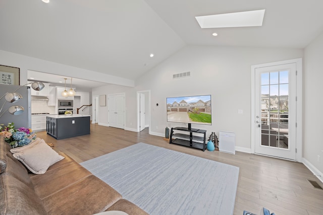 living room featuring lofted ceiling with skylight, visible vents, and light wood-style floors