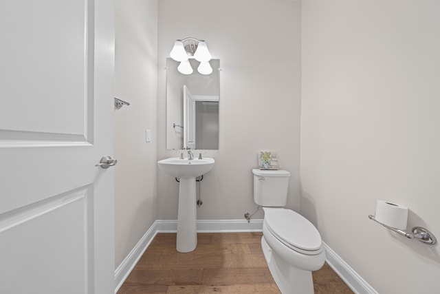 half bath with toilet, wood finished floors, and baseboards