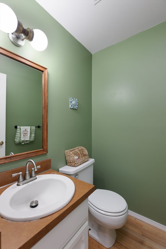 half bathroom featuring toilet, baseboards, vanity, and wood finished floors