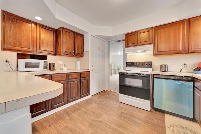 kitchen with brown cabinets, light wood finished floors, white appliances, light countertops, and under cabinet range hood