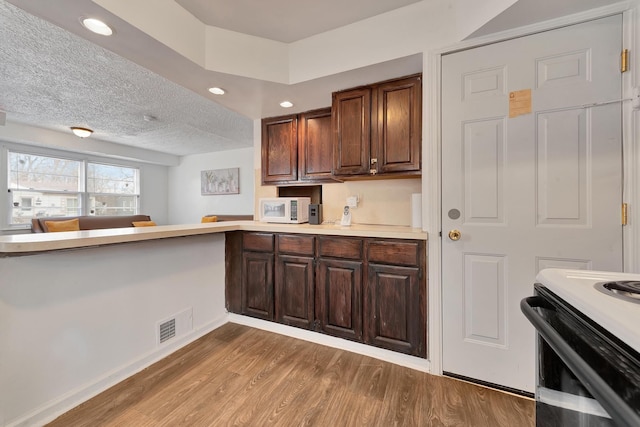 kitchen with a peninsula, baseboards, white microwave, light countertops, and light wood finished floors