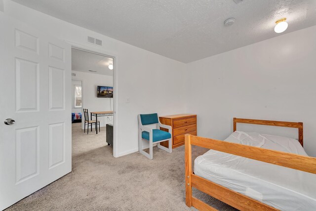 bedroom with visible vents, a textured ceiling, baseboards, and light colored carpet