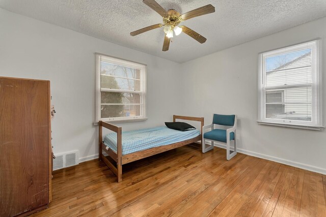 bedroom with ceiling fan, light wood finished floors, a textured ceiling, baseboards, and visible vents