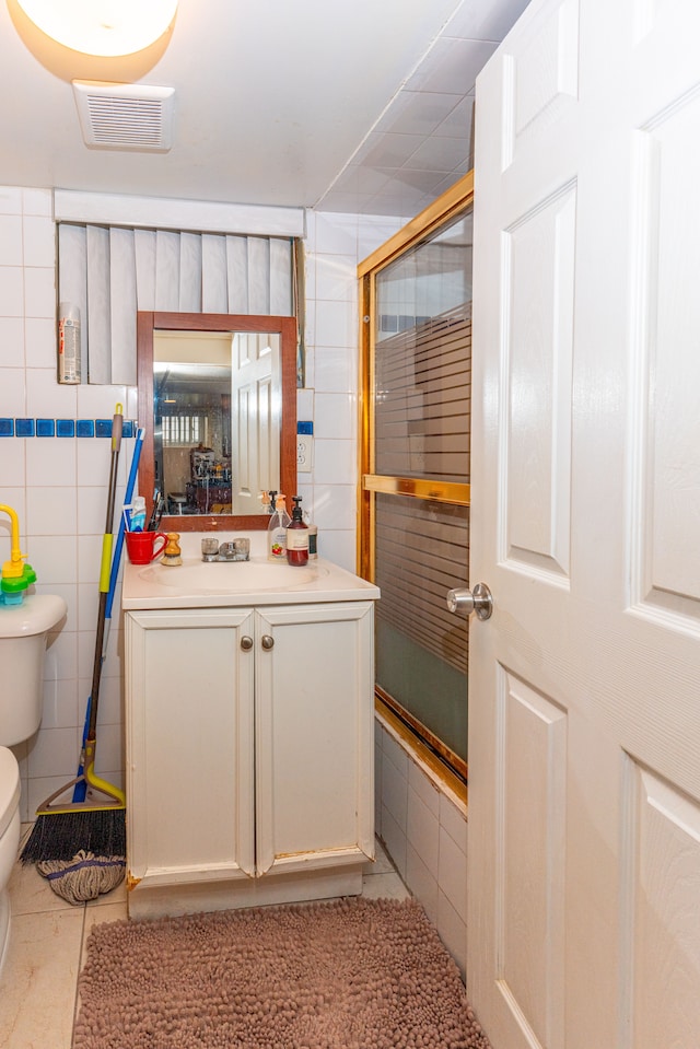 bathroom with visible vents, vanity, toilet, and tile walls