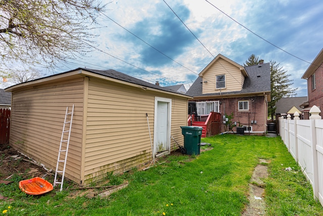 rear view of house with a lawn, brick siding, cooling unit, an outdoor structure, and a fenced backyard