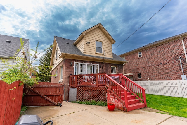back of house featuring fence, roof with shingles, brick siding, a gate, and a patio area