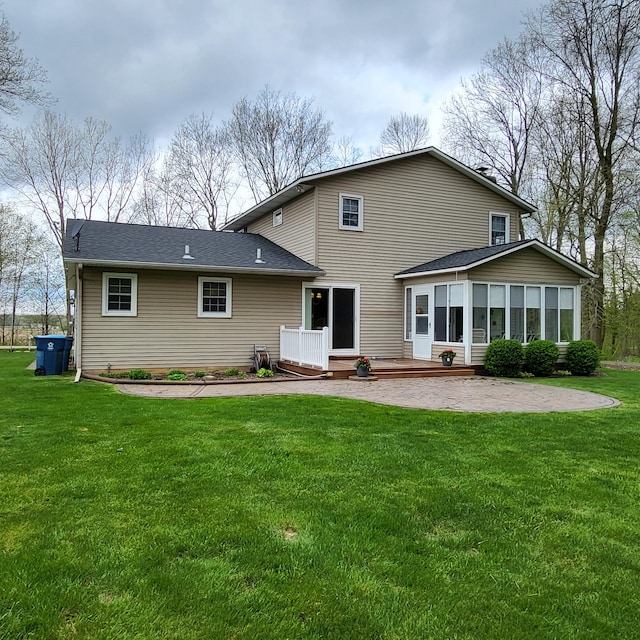 back of house with a sunroom, a yard, a wooden deck, roof with shingles, and a patio
