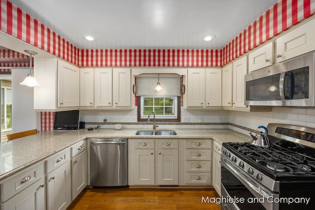 kitchen with appliances with stainless steel finishes, a sink, decorative backsplash, light stone counters, and dark wood-style floors