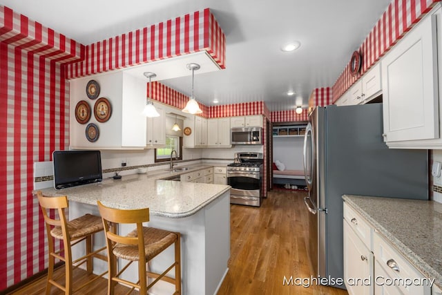 kitchen featuring stainless steel appliances, wallpapered walls, a sink, a peninsula, and wood finished floors