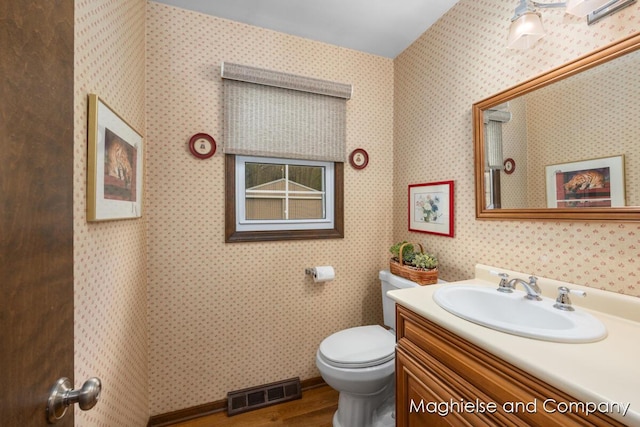 bathroom with toilet, vanity, wood finished floors, and wallpapered walls