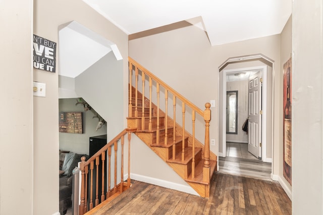 staircase with arched walkways, baseboards, and wood finished floors