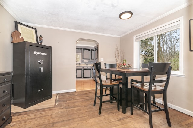 dining area with crown molding, arched walkways, light wood-type flooring, and baseboards