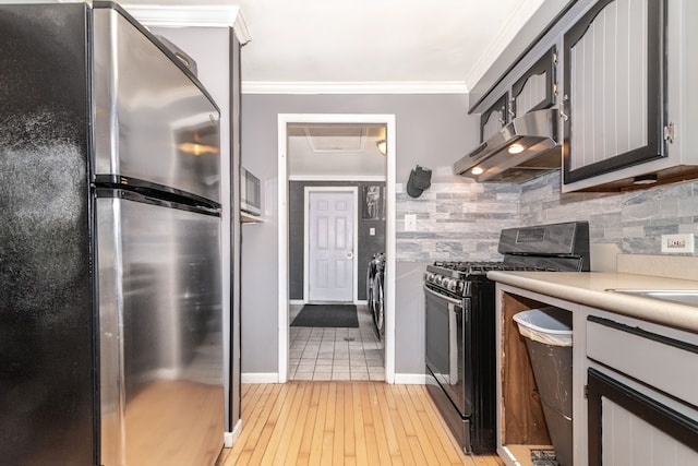 kitchen featuring tasteful backsplash, freestanding refrigerator, under cabinet range hood, gas stove, and light countertops