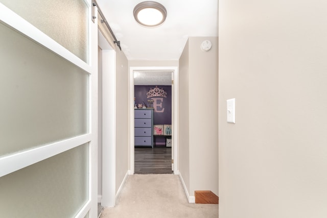 hall with a barn door, light carpet, and baseboards