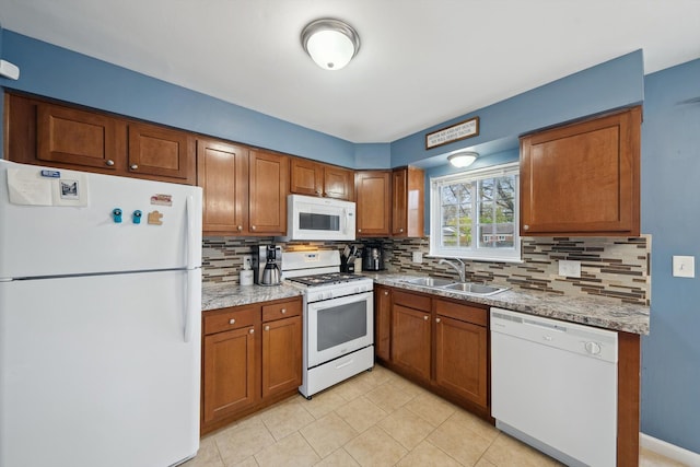 kitchen featuring brown cabinets, tasteful backsplash, a sink, and white appliances