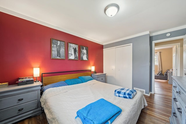bedroom featuring a closet, dark wood finished floors, visible vents, baseboards, and ornamental molding