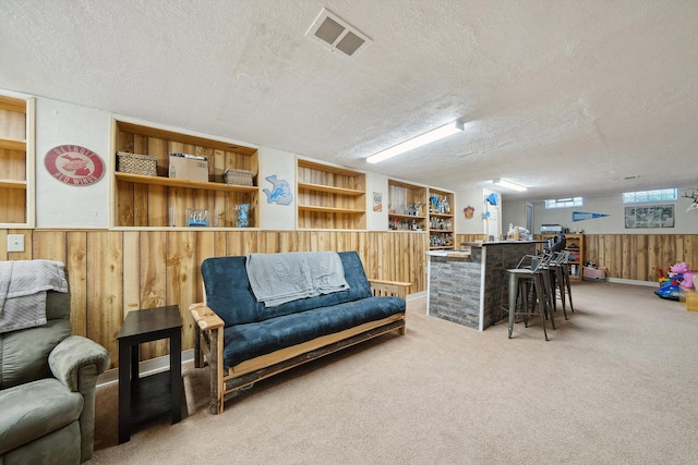 living area with light carpet, a textured ceiling, wooden walls, and visible vents