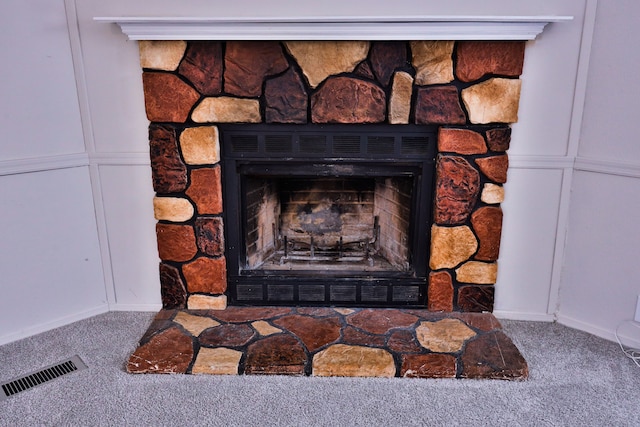 detailed view of carpet floors, a stone fireplace, baseboards, and a decorative wall