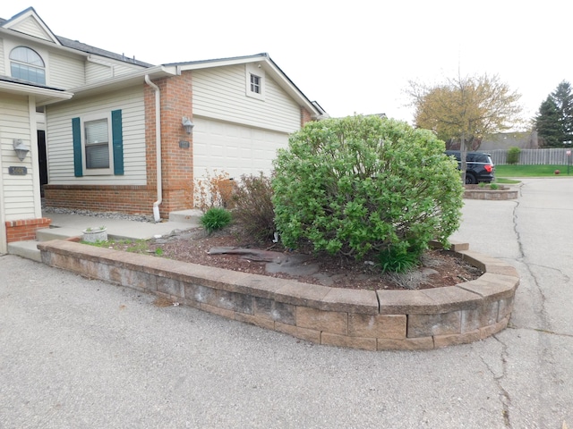 view of property exterior with brick siding, an attached garage, and fence