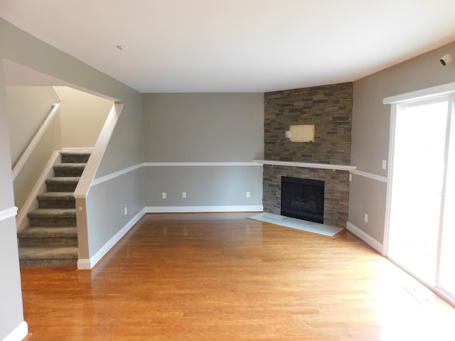 unfurnished living room featuring stairway, a stone fireplace, baseboards, and light wood finished floors