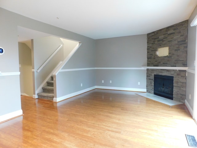 unfurnished living room featuring light wood finished floors, a stone fireplace, stairs, baseboards, and visible vents