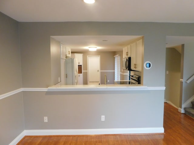 kitchen with white cabinets, stainless steel appliances, a peninsula, and wood finished floors